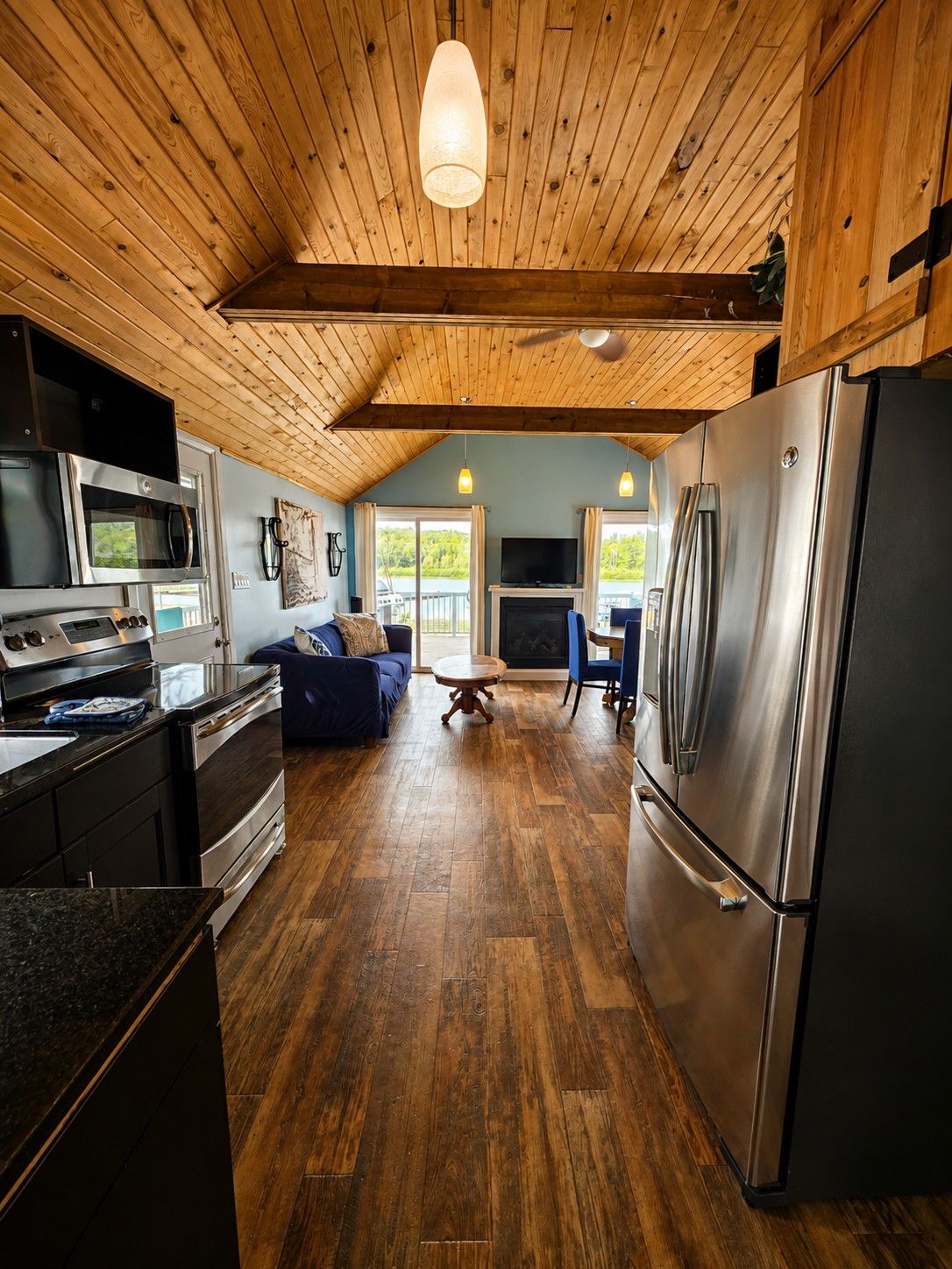 A modern kitchen with a large refrigerator, microwave, and stove. There is a dining area with a table and chairs, and a blue sofa.