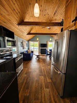 A modern kitchen with a large refrigerator, microwave, and stove. There is a dining area with a table and chairs, and a blue sofa. - Echo Beach Cottage Resort (Magnetawan)