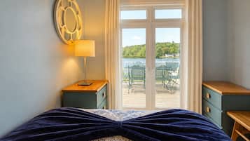 Un dormitorio con cama, mesita de noche, lámpara, ventana con cortinas y vista a un patio exterior.