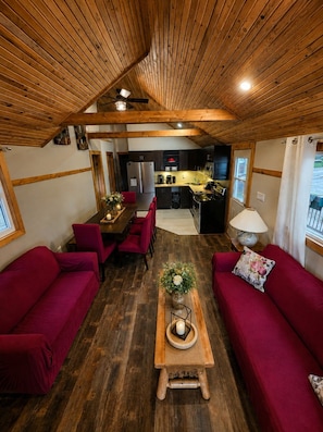 A cozy interior with a wooden ceiling, a dining area with red chairs, a kitchen with modern appliances, and a red sofa.