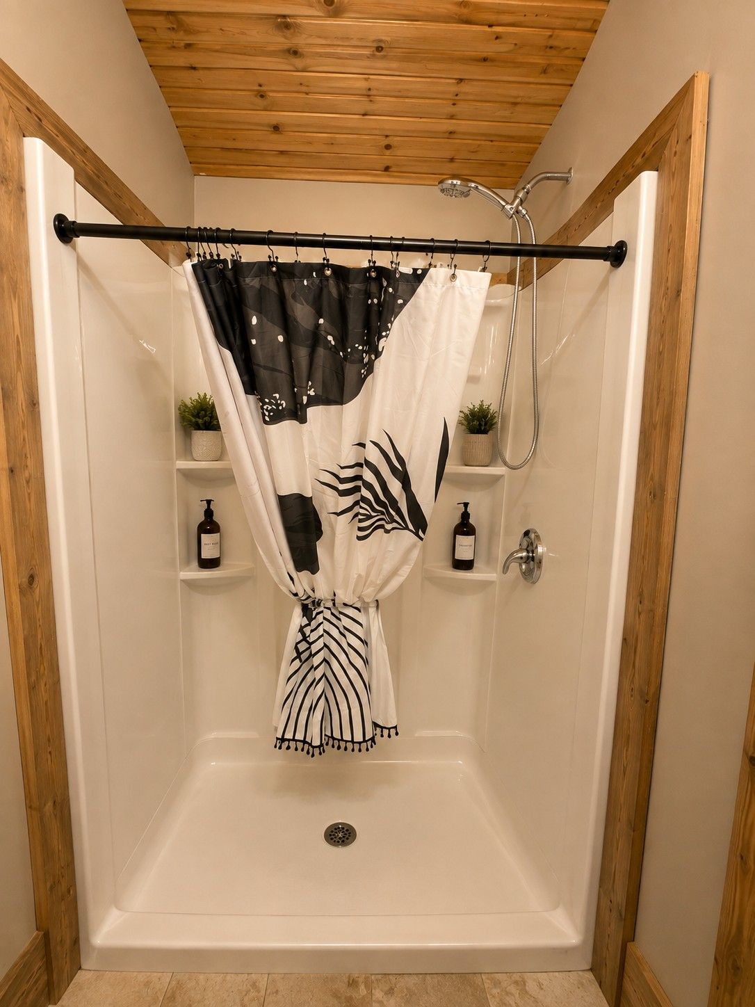 Ducha a nivel con techo de madera, cortina de baño blanco y negro, y dos plantas pequeñas en estantes.