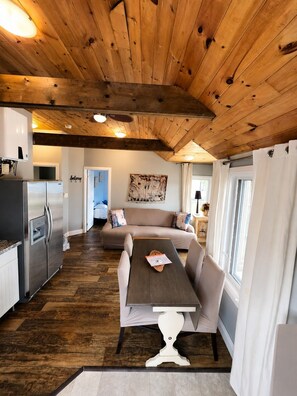 Un intérieur chaleureux avec un plafond en bois, une table à manger avec des chaises, un canapé et un coin cuisine équipé d’un réfrigérateur.