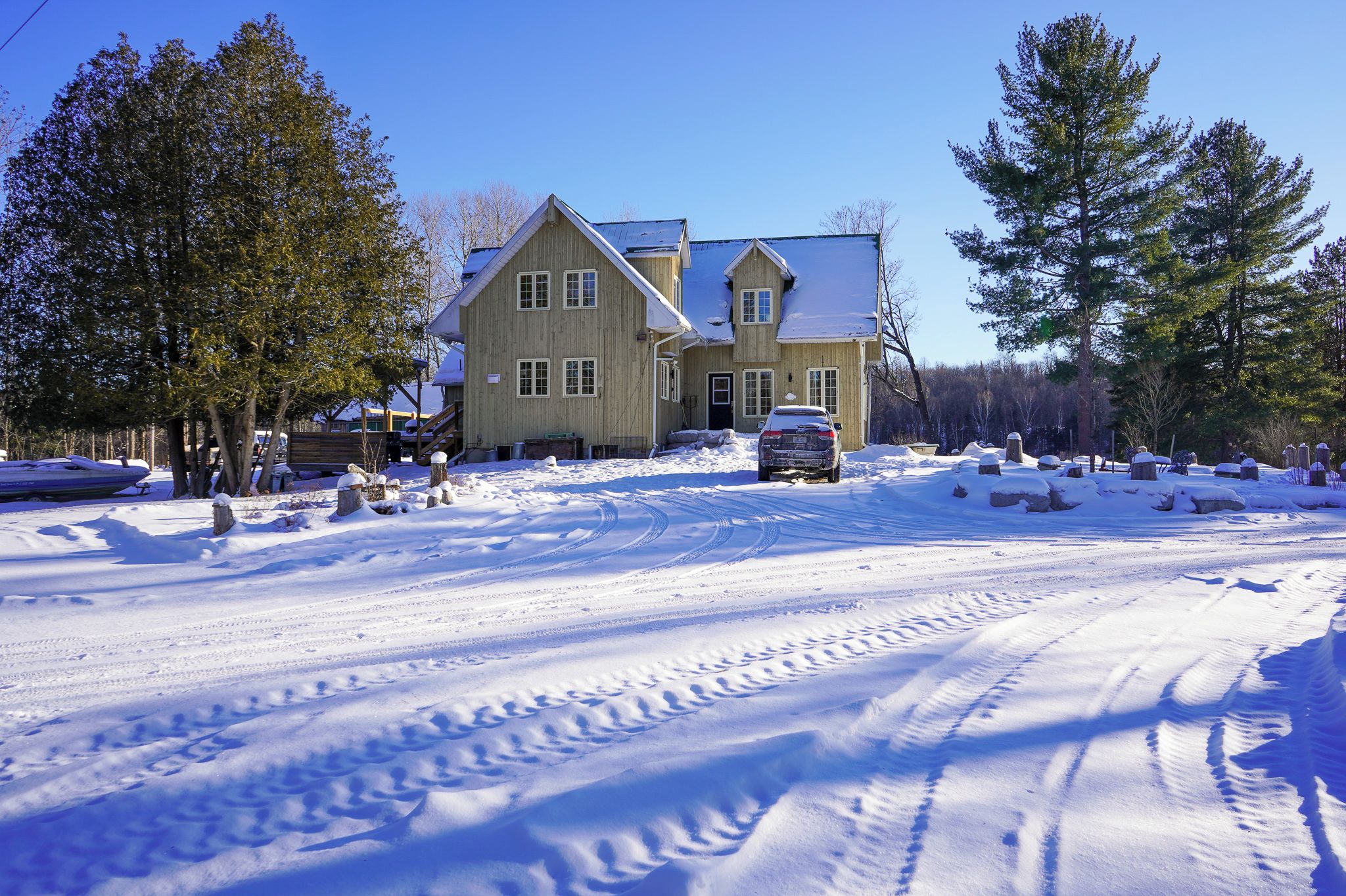 A two-story wooden house with a snow-covered driveway and a car parked in front.
