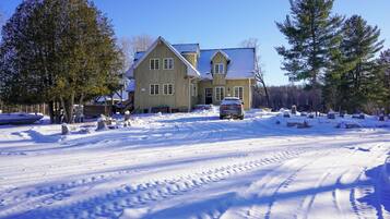 A two-story wooden house with a snow-covered driveway and a car parked in front.