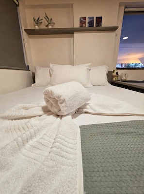 Habitación de hotel con cama, almohadas, una toalla blanca doblada, una alfombra de textura verde y una ventana con vistas.