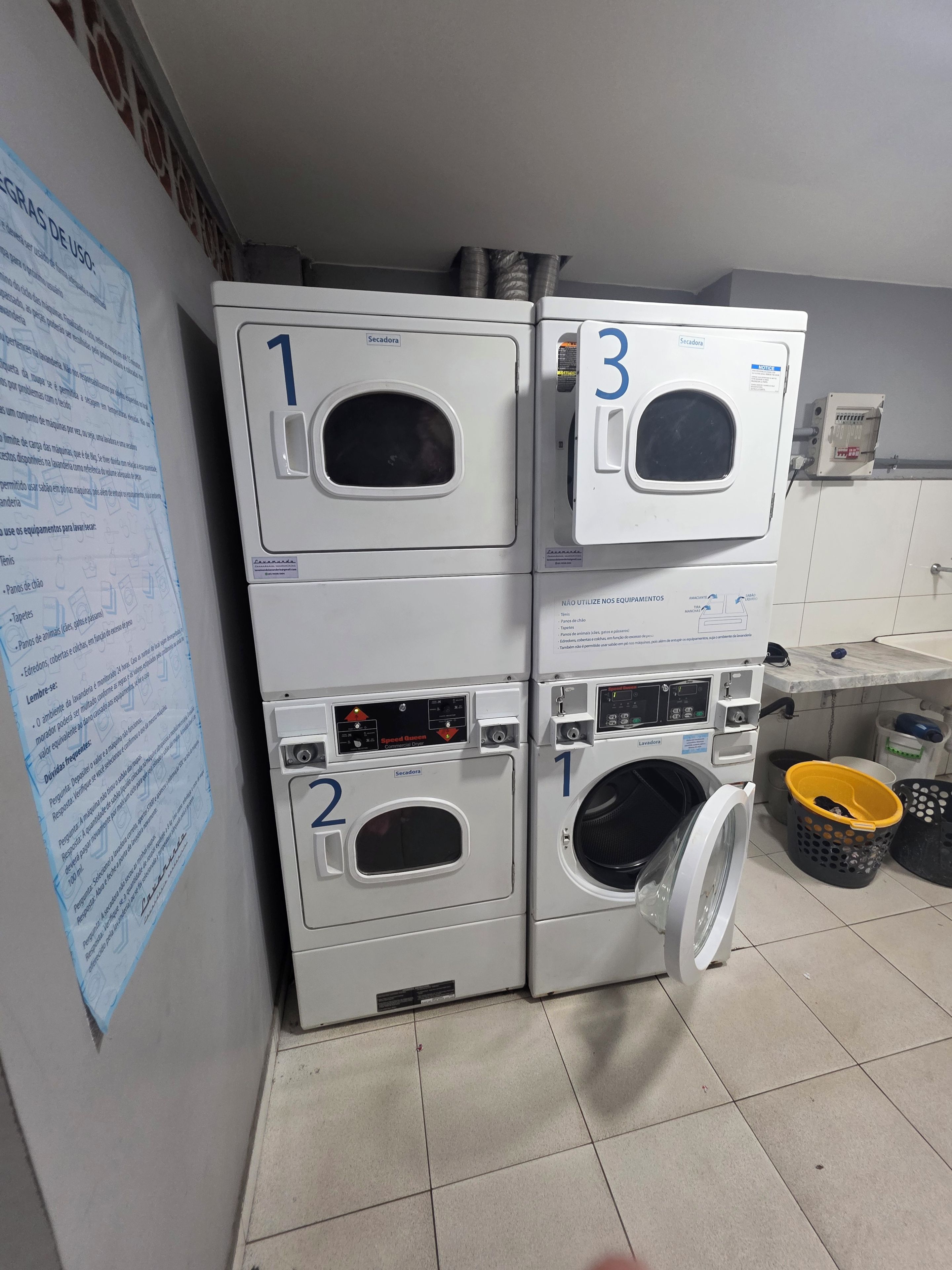 A laundry area with three stacked washing machines, numbered 1, 2, and 3, and a notice board with instructions.