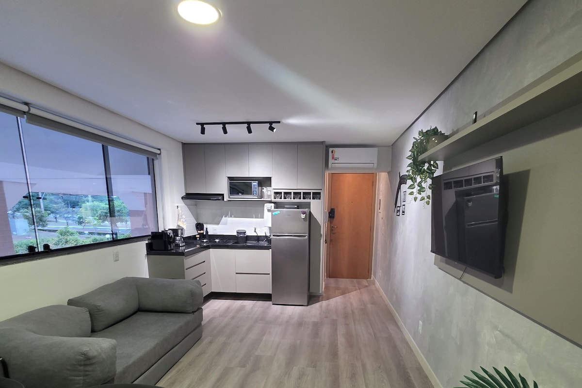 A modern kitchen with a refrigerator, microwave, and sink. There is a gray sofa and a small table with a remote control.