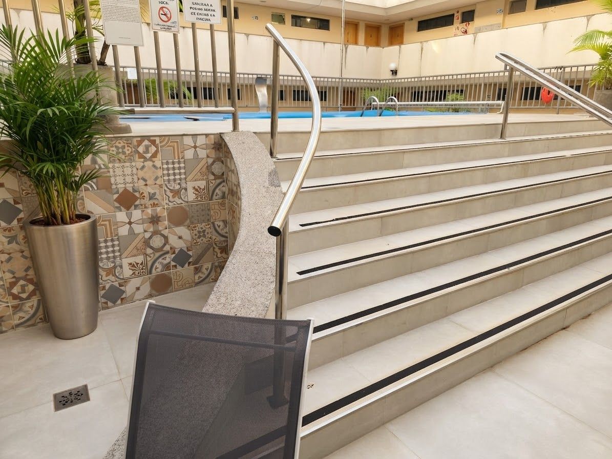 A pool area with steps leading to a pool, a potted plant, and a tiled wall with a geometric pattern.