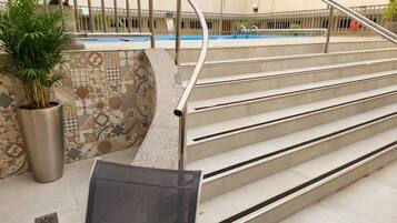 A pool area with steps leading to a pool, a potted plant, and a tiled wall with a geometric pattern.
