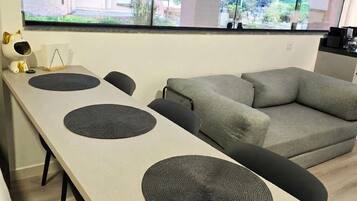 Uma sala de estar moderna com uma mesa comprida, dois sofás e uma janela grande com vista para prédios.