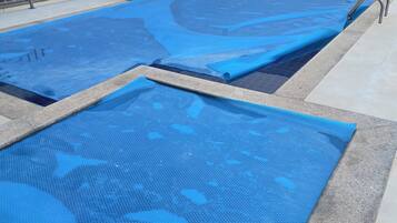 Piscina com tapetes azuis cobrindo a superfície, grade de metal e um edifício ao fundo.