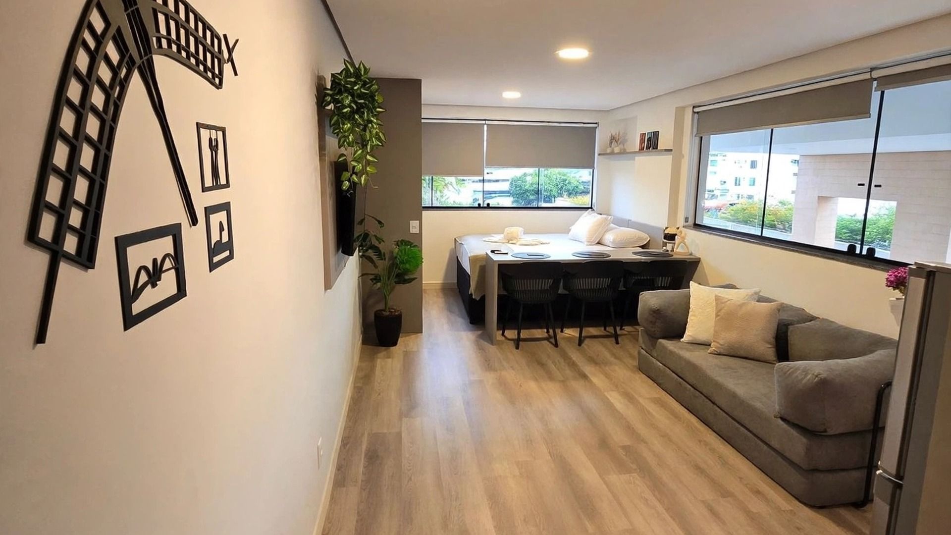 Una sala de estar moderna con un sofá, una mesa de comedor y sillas. Hay plantas, un televisor y obras de arte en las paredes.