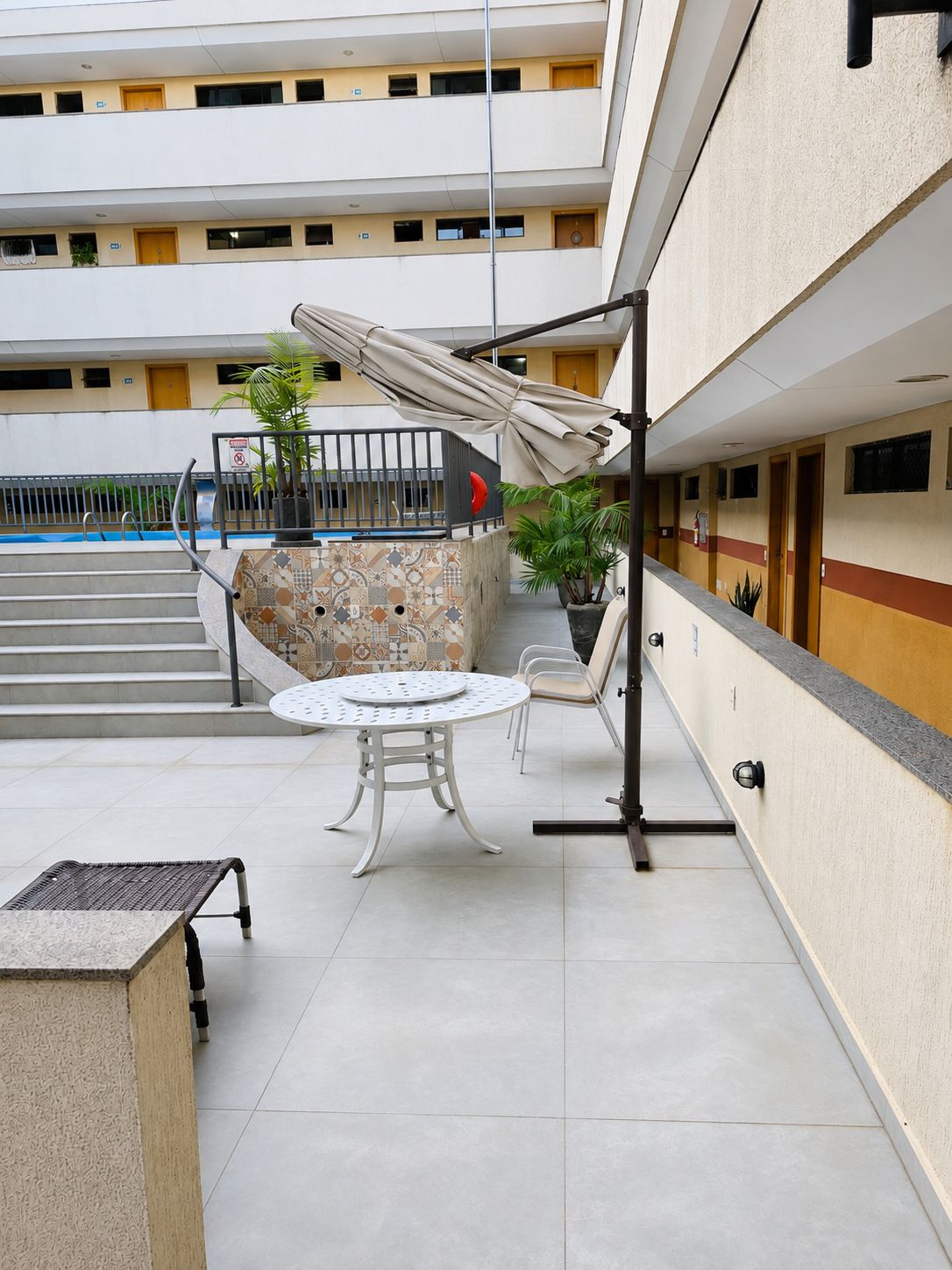 A covered outdoor seating area with a pool, steps leading to a building, and a railing.