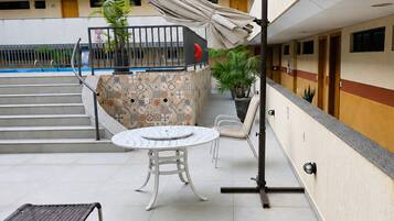 A covered outdoor seating area with a pool, steps leading to a building, and a railing.