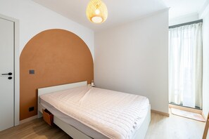A bedroom with a single bed, a door, a light fixture, and a window with curtains. - Penthouse by the Sea With Stunning Rooftop Views (Blankenberge)