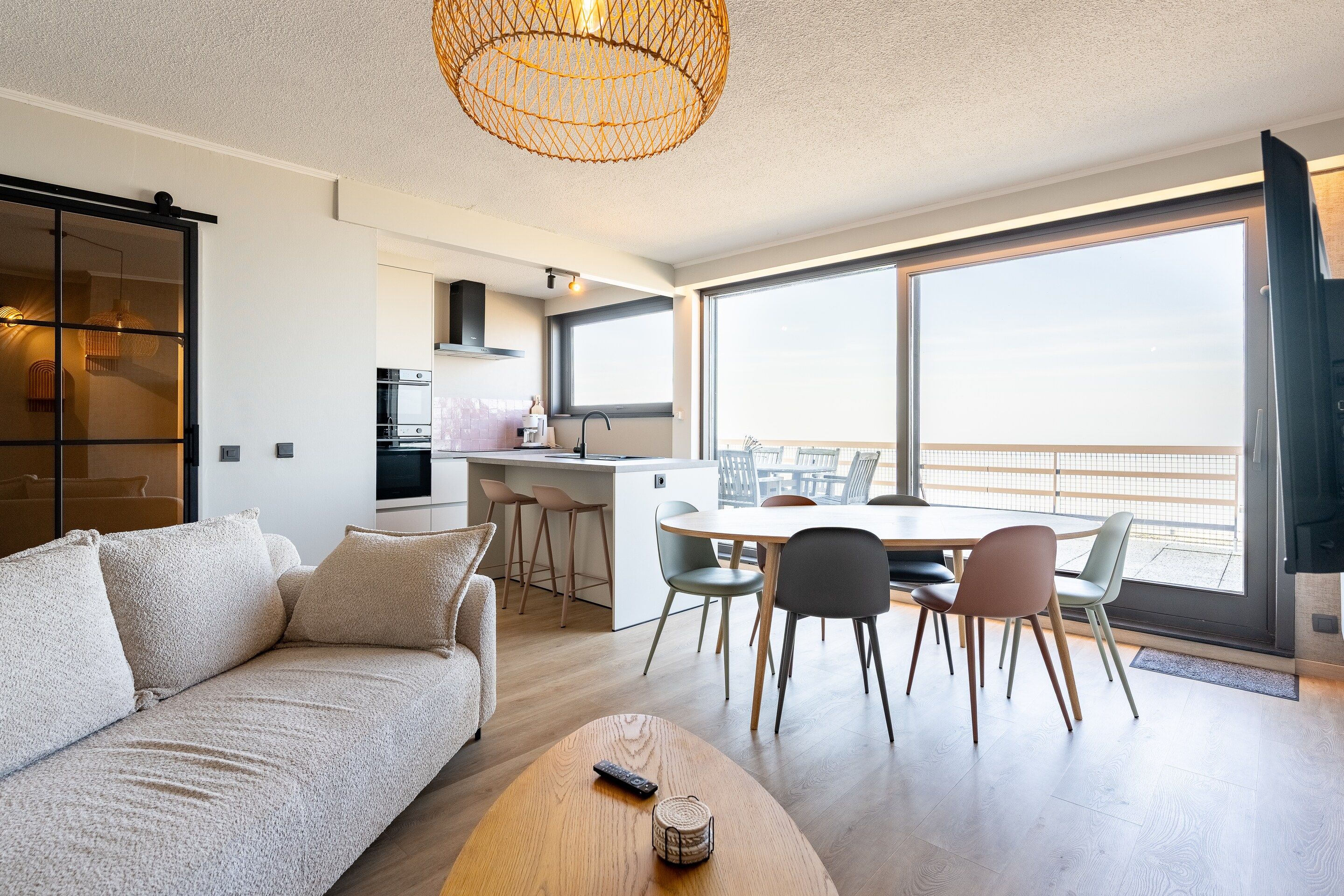 A modern living space with a sofa, a dining table with chairs, a kitchen area, and large windows offering a view.