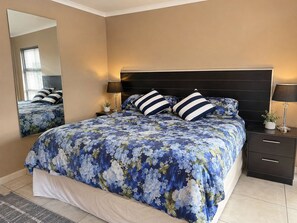 A bedroom with a large bed, a nightstand, a mirror, and a lamp.