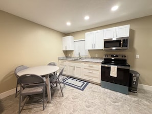 A compact kitchen with white cabinets, a microwave, an oven, and a sink. There is a dining table with chairs. - Cozy 2BR/1BA house in lovely Bradenton 25 minutes from Beaches (Bradenton)
