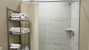 Et badeværelse med bruser, toilet og et håndklædestativ med foldede håndklæder.