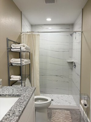 A bathroom with a shower, toilet, and a towel rack with folded towels. - Cozy 2BR/1BA house in lovely Bradenton 25 minutes from Beaches (Bradenton)