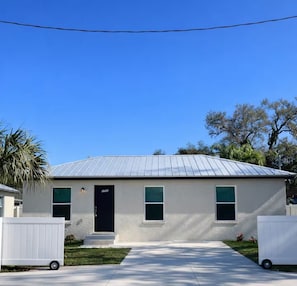 A single-story building with a metal roof, a black door, and two windows with green shutters. - Cozy 2BR/1BA house in lovely Bradenton 25 minutes from Beaches (Bradenton)