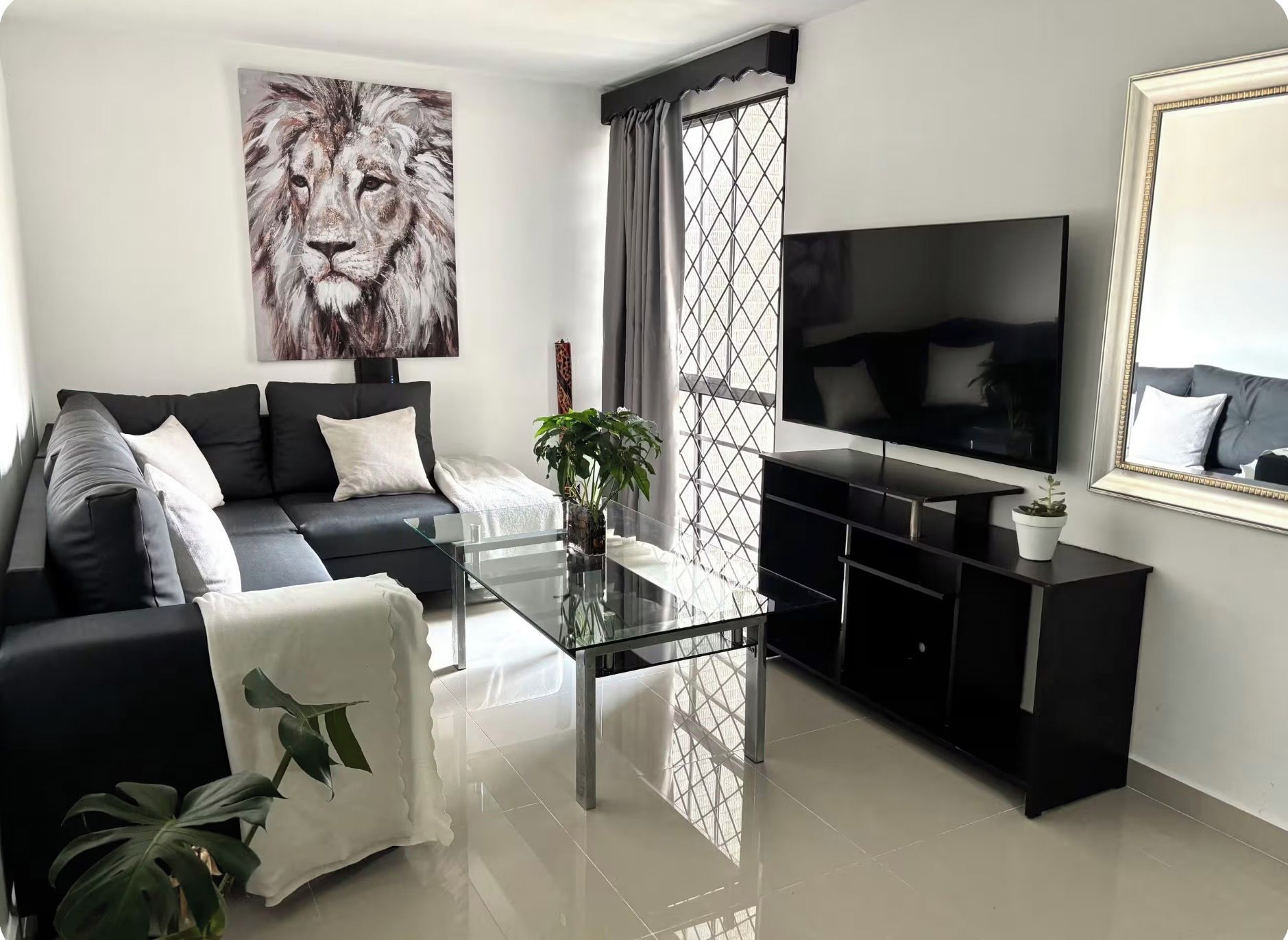 Una sala de estar moderna con un sofá negro, una mesa de centro de vidrio, un televisor grande y un cuadro de un león.
