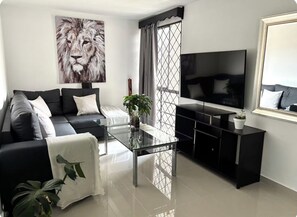 A modern living room with a black sofa, a glass coffee table, a large TV, and a painting of a lion. - Apartment near the town of Medellín (Medellín)