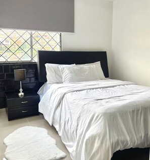 A bedroom with a bed, a nightstand, a lamp, and a view through a window. - Apartment near the town of Medellín (Medellín)