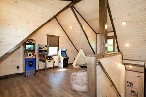 Ein Zimmer mit schrägem Dach, Holzwänden, Spielautomaten, einem Zelt und einem Fenster.
