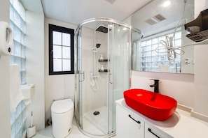 Casa de banho moderna com cabine de duche em vidro, sanita branca e lavatório vermelho.