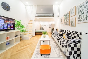Uma sala de estar moderna com um sofá, um banquinho e uma TV de tela plana.