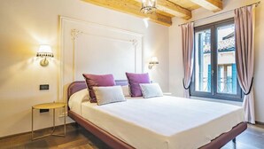 A bedroom with a large bed, two bedside lamps, a small round table, and a window with curtains. - ELEGANT CORTE RUBBI 2-BEDROOM RETREAT STEPS FROM ST. MARK'S SQUARE (Venezia)