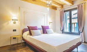Une chambre à coucher avec un grand lit, deux lampes de chevet, une petite table ronde et une fenêtre avec des rideaux.