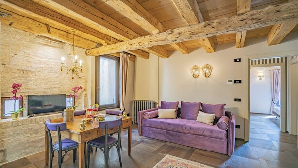 A cozy living room with a wooden ceiling, a purple sofa, a dining table with chairs, and a TV. - ELEGANT CORTE RUBBI 2-BEDROOM RETREAT STEPS FROM ST. MARK'S SQUARE (Venezia)