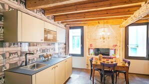 A modern kitchen with a central island, a dining area with a table and chairs, and a stone wall in the background. - ELEGANT CORTE RUBBI 2-BEDROOM RETREAT STEPS FROM ST. MARK'S SQUARE (Venezia)