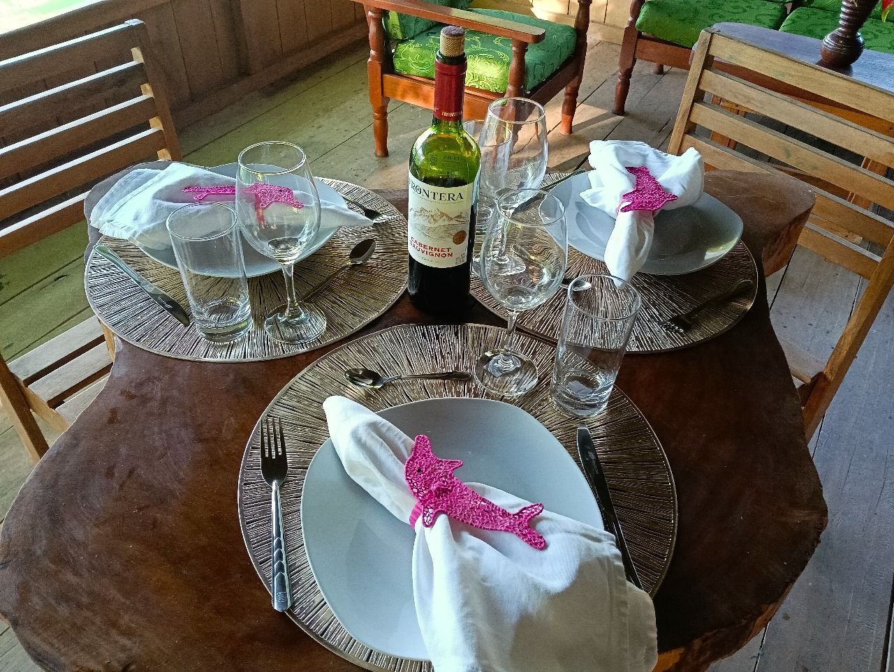 Uma mesa de jantar posta com pratos, talheres e copos de vinho, com uma garrafa de vinho ao centro.