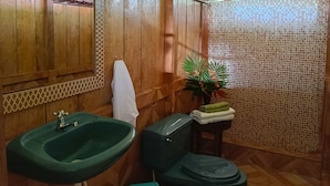 Un baño con paredes de madera, un lavabo verde, un inodoro y una zona de ducha.
