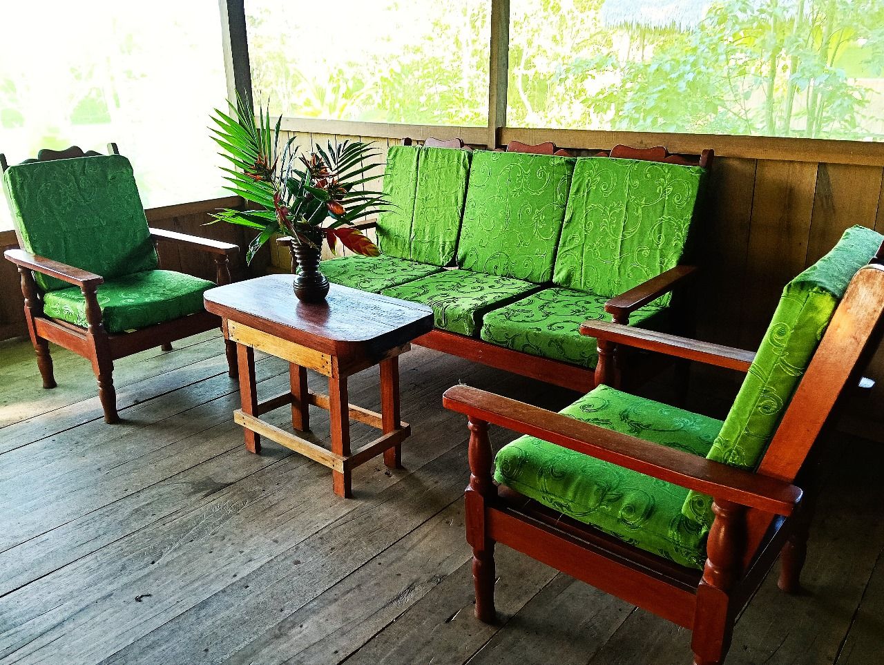 Un porche de madera con sillas acolchadas de color verde y una pequeña mesa.