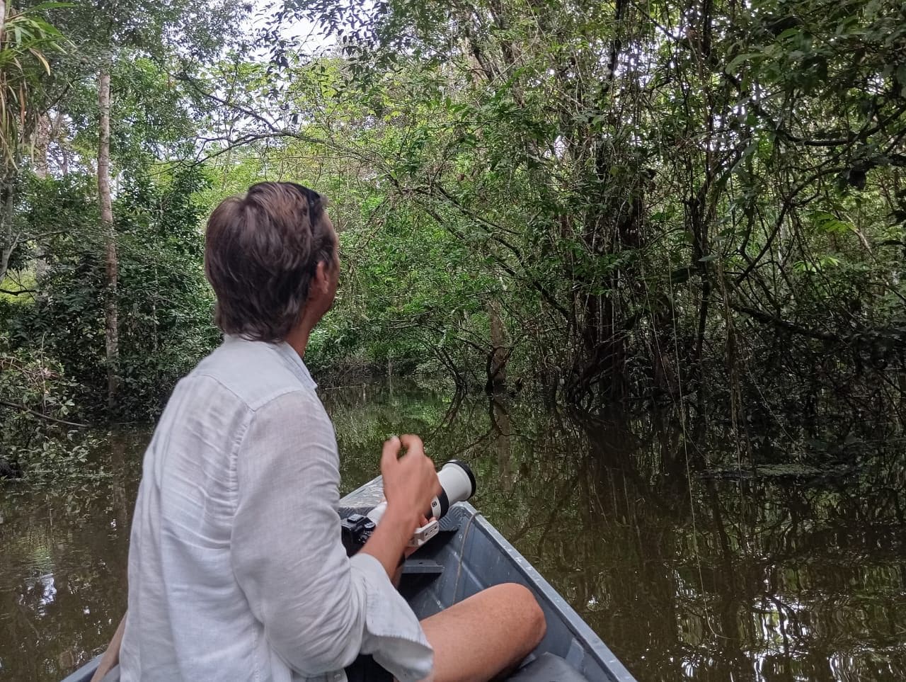 Una persona en un bote con una cámara, rodeada de abundante vegetación y agua.