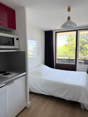 A compact room with a bed, kitchenette, and a window with a view of greenery. - Studio for 4 – Résidence Les Marmottes – 1750 Chamrousse (Chamrousse)