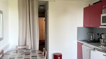 Una cocina compacta con comedor, un bote de basura rojo y una lámpara en el techo.