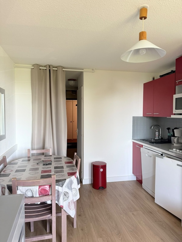 A compact kitchen with a dining area, a red trash bin, and a ceiling light fixture. - Studio for 4 – Résidence Les Marmottes – 1750 Chamrousse (Chamrousse)