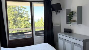 Habitación de hotel con una cama, un escritorio con computadora, televisión y vistas a árboles a través de la ventana.