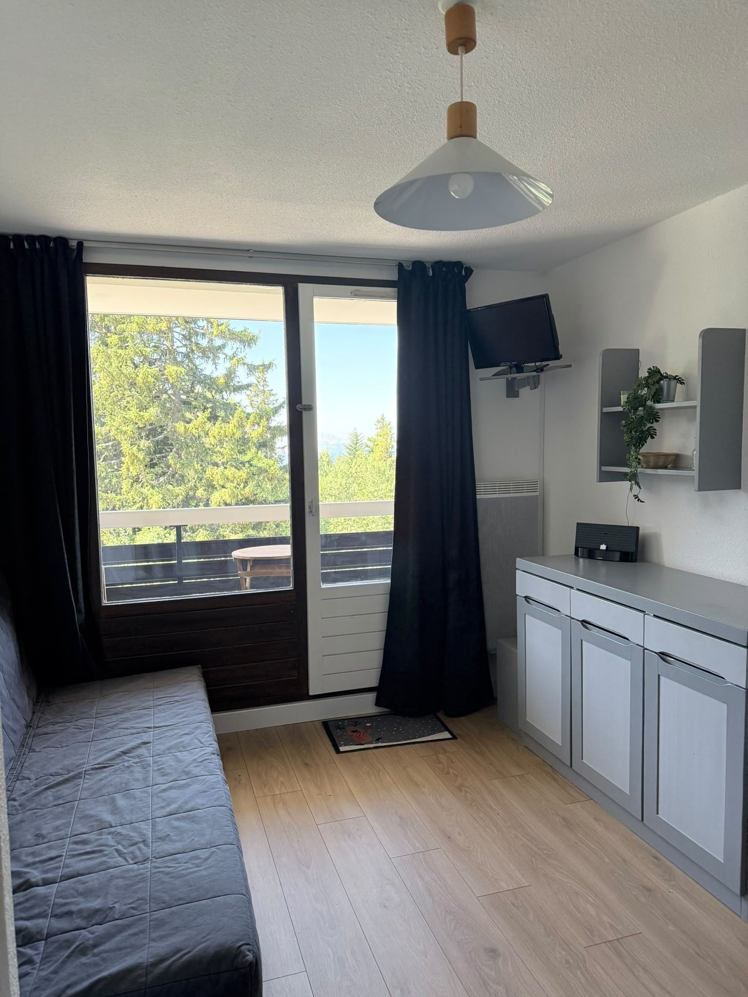 Una habitación con una cama, un televisor montado en la pared, una kitchenette pequeña y una puerta corrediza de vidrio que da a un espacio al aire libre.