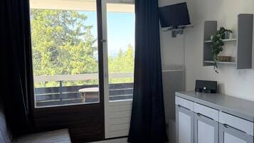 Una habitación con una cama, un televisor montado en la pared, una kitchenette pequeña y una puerta corrediza de vidrio que da a un espacio al aire libre.