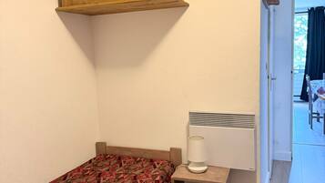 Un dormitorio con una cama, una mesita de noche pequeña, un calentador y un armario de madera sobre la cama.
