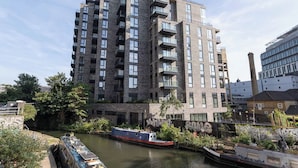 Un immeuble à plusieurs étages doté de balcons, avec une rivière et un bateau amarré à proximité.