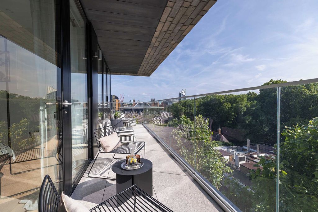 Un balcon moderne avec des garde-corps en verre, un espace salon extérieur et une vue dégagée sur le paysage urbain.