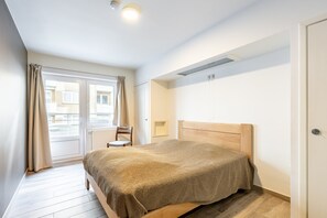 Ein Schlafzimmer mit einem Bett, einem Sessel, einem Fenster mit Vorhängen und einer Heizung.