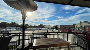 Un balcon extérieur donnant sur un parking et des immeubles, avec une table en bois et une chaise en osier.